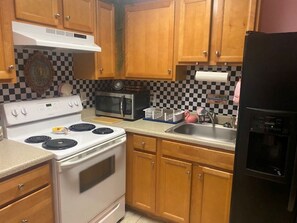 A kitchen with wooden cabinets, a white stove, a black refrigerator, and a microwave. - Enjoy the pool, relax by the fire pit, or spend time exploring North Georgia! (Oakwood)