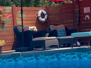 A poolside area with a lounge chair, a small table, and a life preserver on a wooden fence. - Enjoy the pool, relax by the fire pit, or spend time exploring North Georgia! (Oakwood)