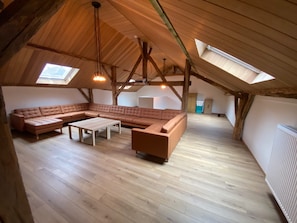 An attic room with a large L-shaped sectional sofa, a small table, and exposed wooden beams. - Detached Holiday Home in La Roche-en-ardenne (La Roche-en-Ardenne)
