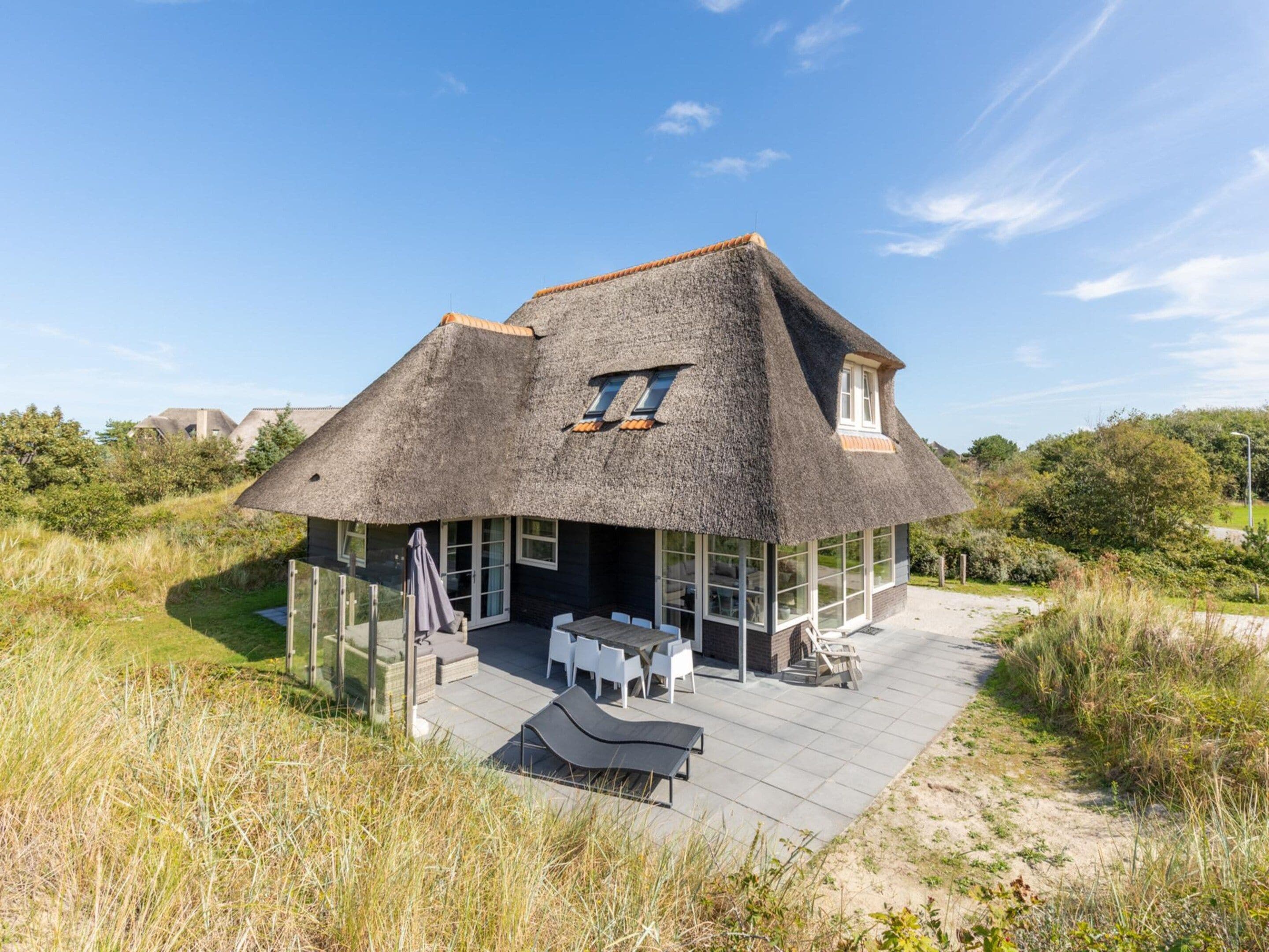 A thatched-roof house with a patio, outdoor seating, and a view of the surrounding landscape.