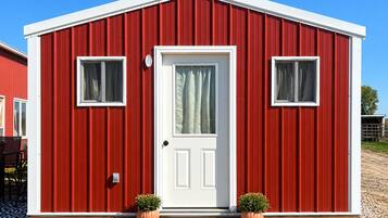 Un bâtiment rouge avec une porte blanche, deux fenêtres et des plantes en pot.