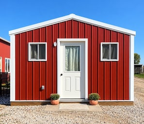 A red building with a white door, two windows, and potted plants. - Beautiful cabin in Brady perfect for a relaxing getaway (Brady)