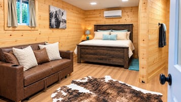 A wooden cabin room with a bed, a leather sofa, a cowhide rug, and a painting of a bull.