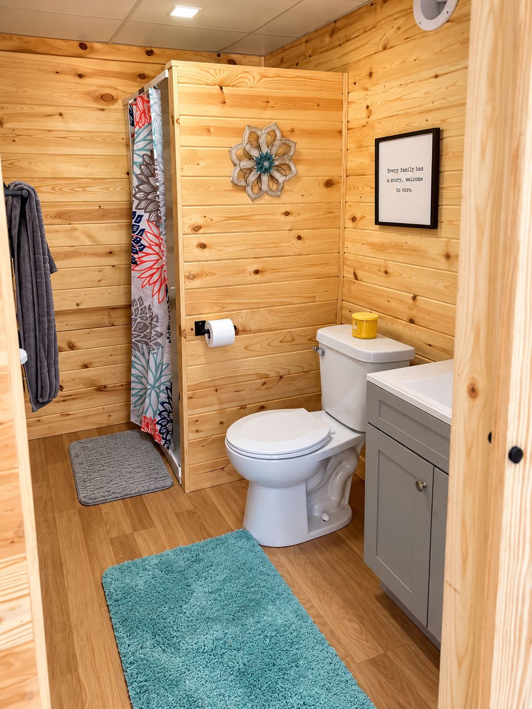 Ein Badezimmer mit Holzvertäfelung, das eine Toilette, ein Waschbecken, einen Handtuchhalter und ein gerahmtes Zitat an der Wand umfasst.
