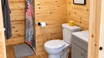 Ein Badezimmer mit Holzvertäfelung, das eine Toilette, ein Waschbecken, einen Handtuchhalter und ein gerahmtes Zitat an der Wand umfasst.