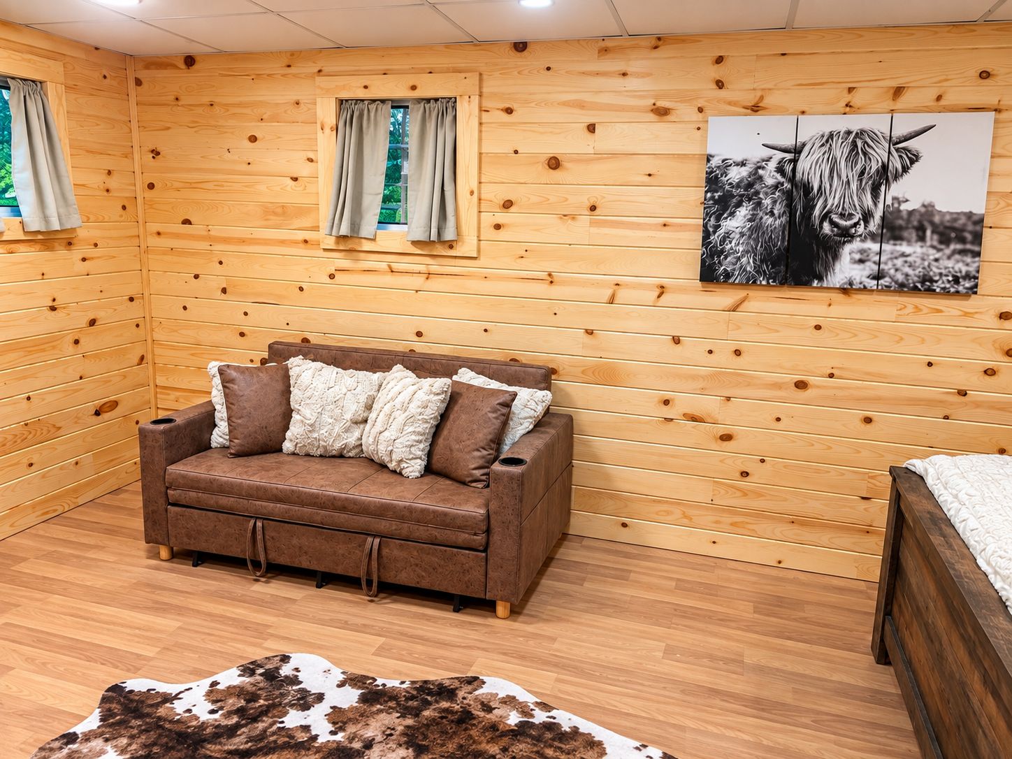 A cozy room with wooden walls, a brown sofa with cushions, a cowhide rug, and a framed picture of a cow.