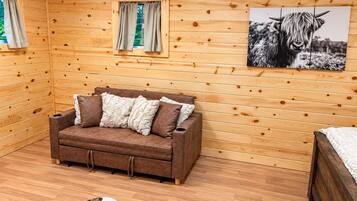 A cozy room with wooden walls, a brown sofa with cushions, a cowhide rug, and a framed picture of a cow.