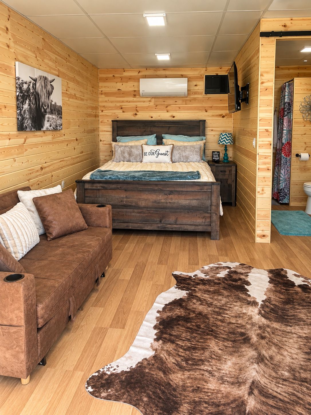 Una habitación acogedora con cama, sofá, piso de madera y alfombra de cuero.