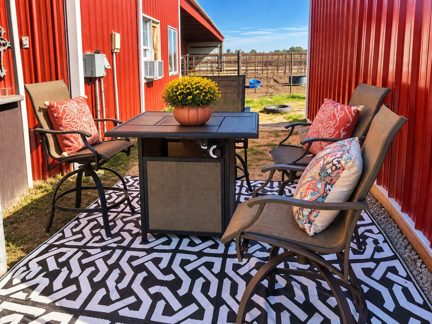 Un patio exterior con una mesa y cuatro sillas, una planta en maceta y un suelo estampado.