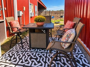 An outdoor patio with a table and four chairs, a potted plant, and a patterned floor.