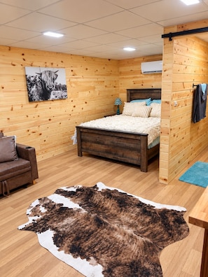 A wooden-paneled room with a bed, a chair, a rug, and a painting on the wall. - Beautiful cabin in Brady perfect for a relaxing getaway (Brady)