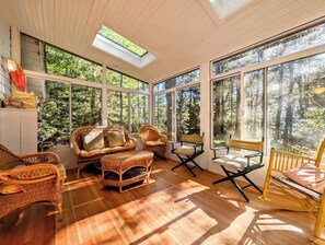 Ein sonnendurchflutetes Zimmer mit großen Fenstern, Korbmöbeln und Holzboden.
