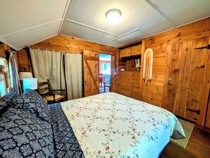 Ein Zimmer aus Holz mit einem Bett, einem Stuhl, einem Tisch und einer Tür, die nach draußen führt.