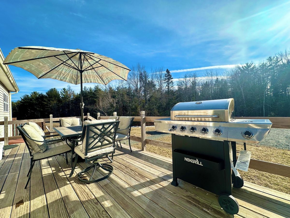 Um terraço com móveis de exterior, churrasqueira e guarda-sol.