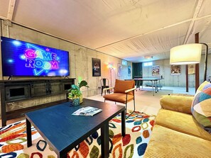 A modern living room with a flat-screen TV, a coffee table, a sofa, and a patterned rug. - Coastal Farmhouse,10 min to beach, game room 1 dog (Lamoine)