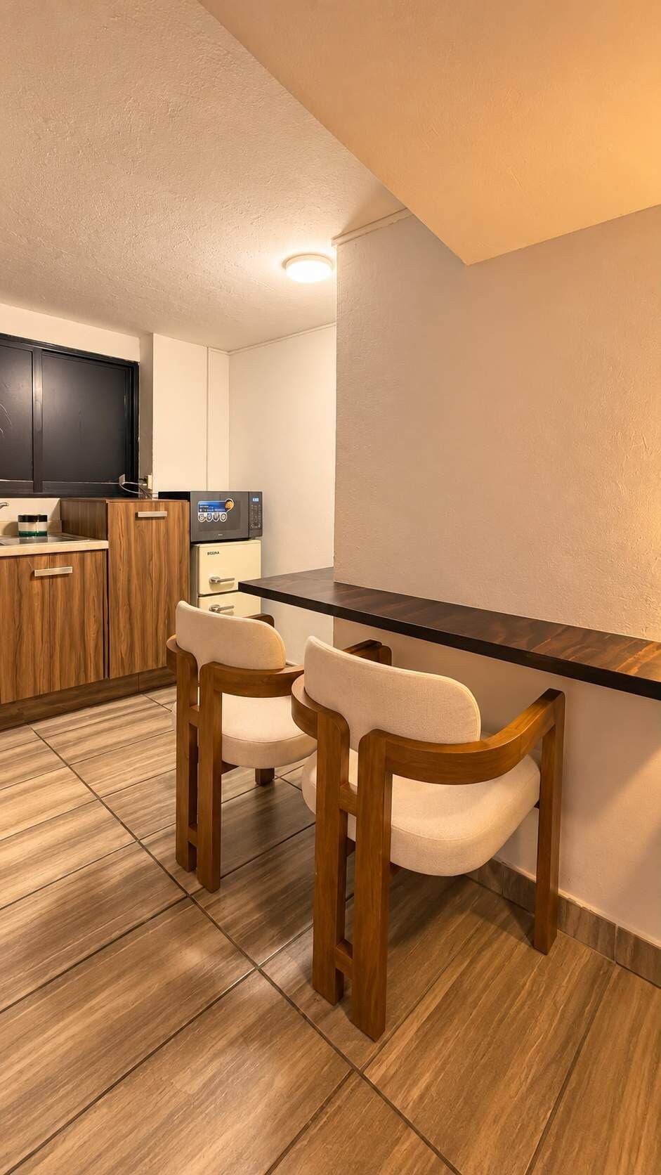 A modern kitchen with wooden cabinets, a microwave, and two upholstered chairs.