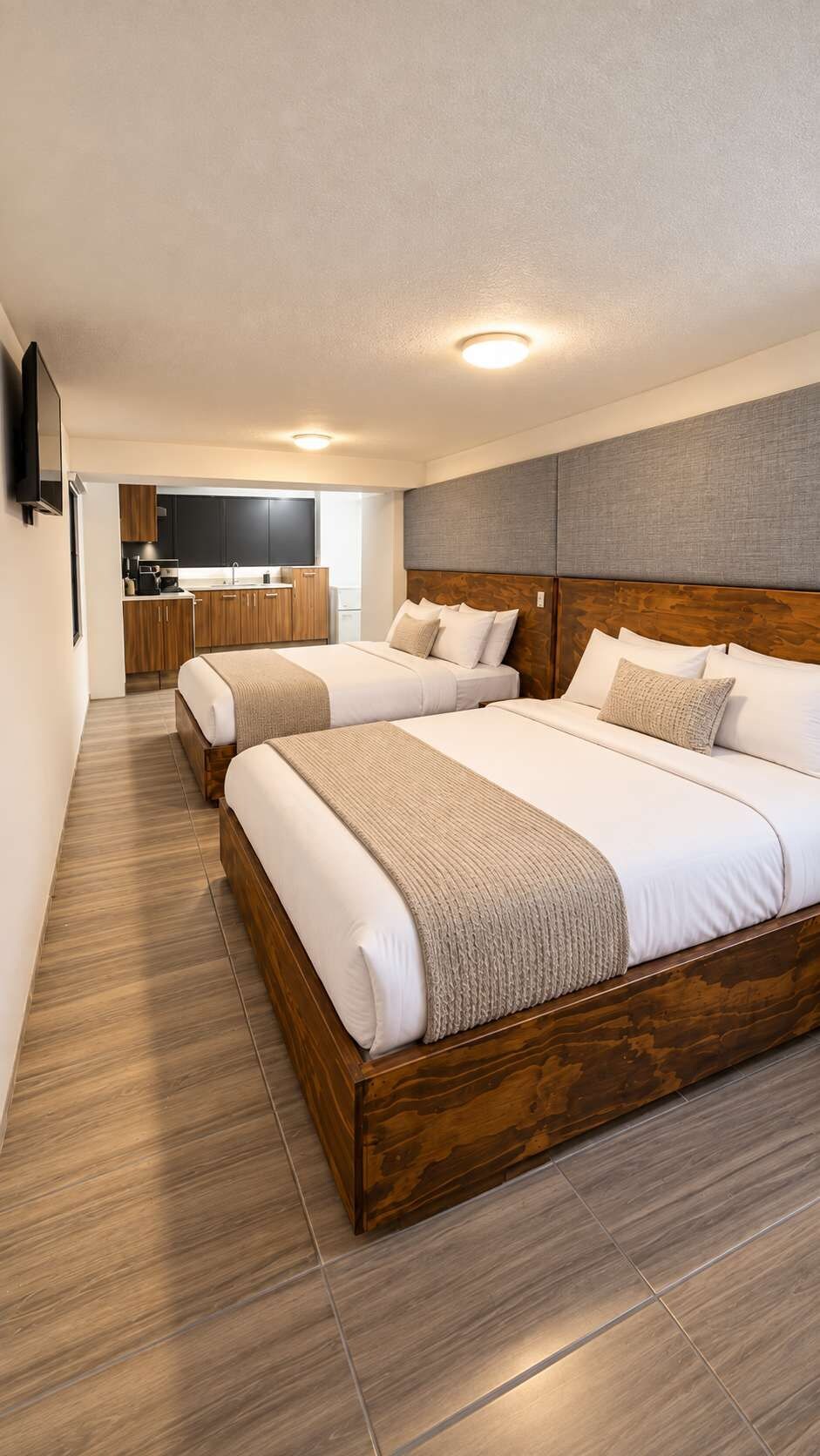 A hotel room with two beds, a kitchenette, and a flat-screen TV.