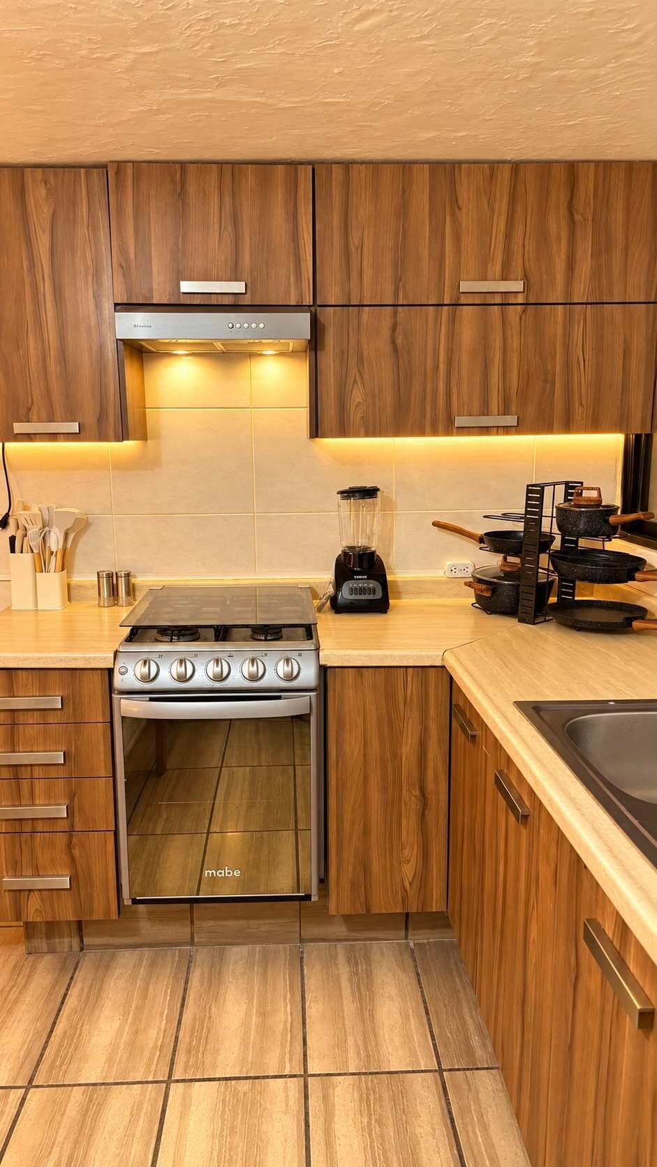 A modern kitchen with wooden cabinets, a gas stove, a built-in oven, and a countertop with a blender.