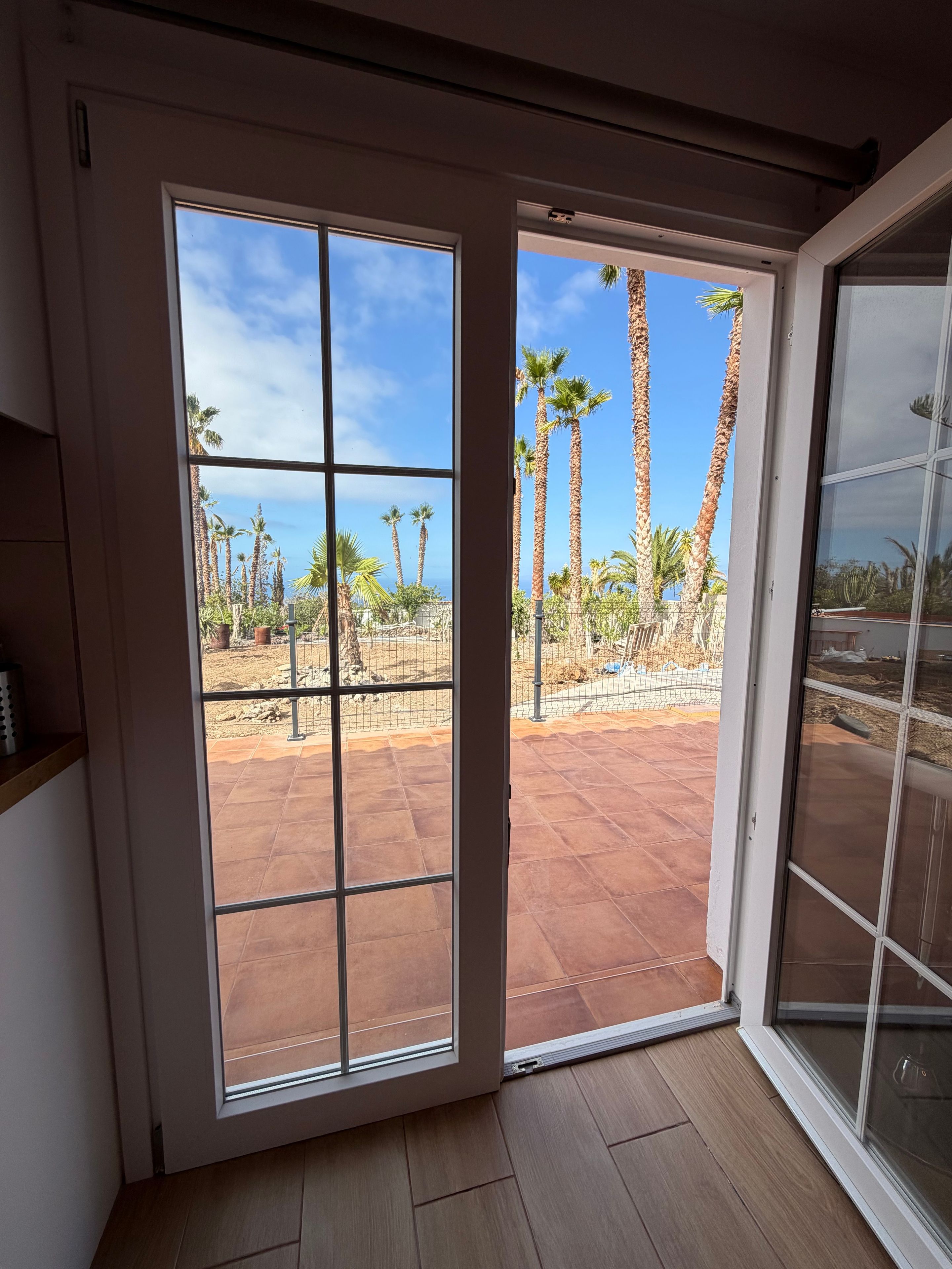 A room with a sliding glass door leading to an outdoor patio with palm trees and a clear sky.