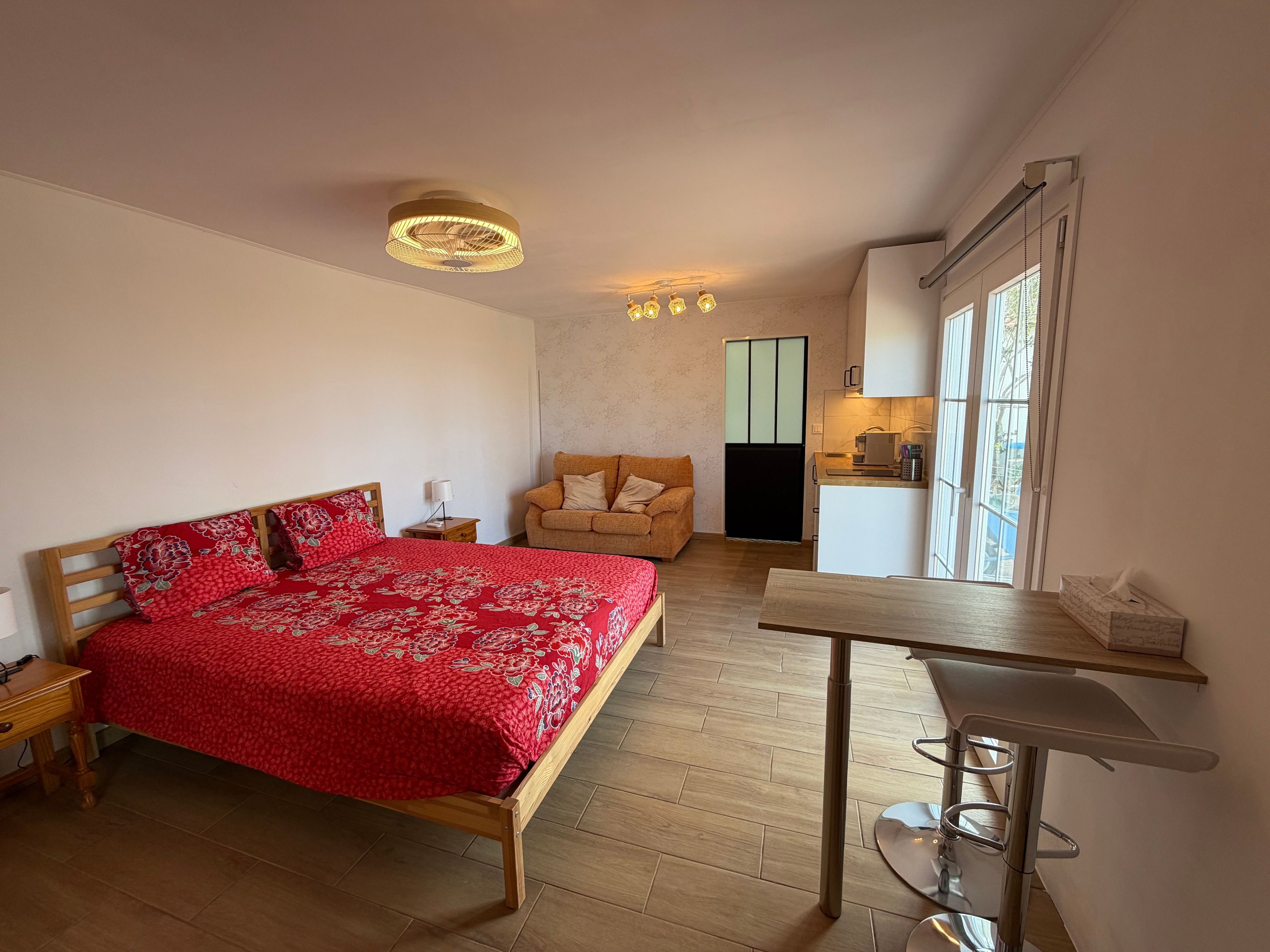 Une chambre comprenant un lit, une table de chevet en bois, une table avec une chaise, un canapé et un coin cuisine.
