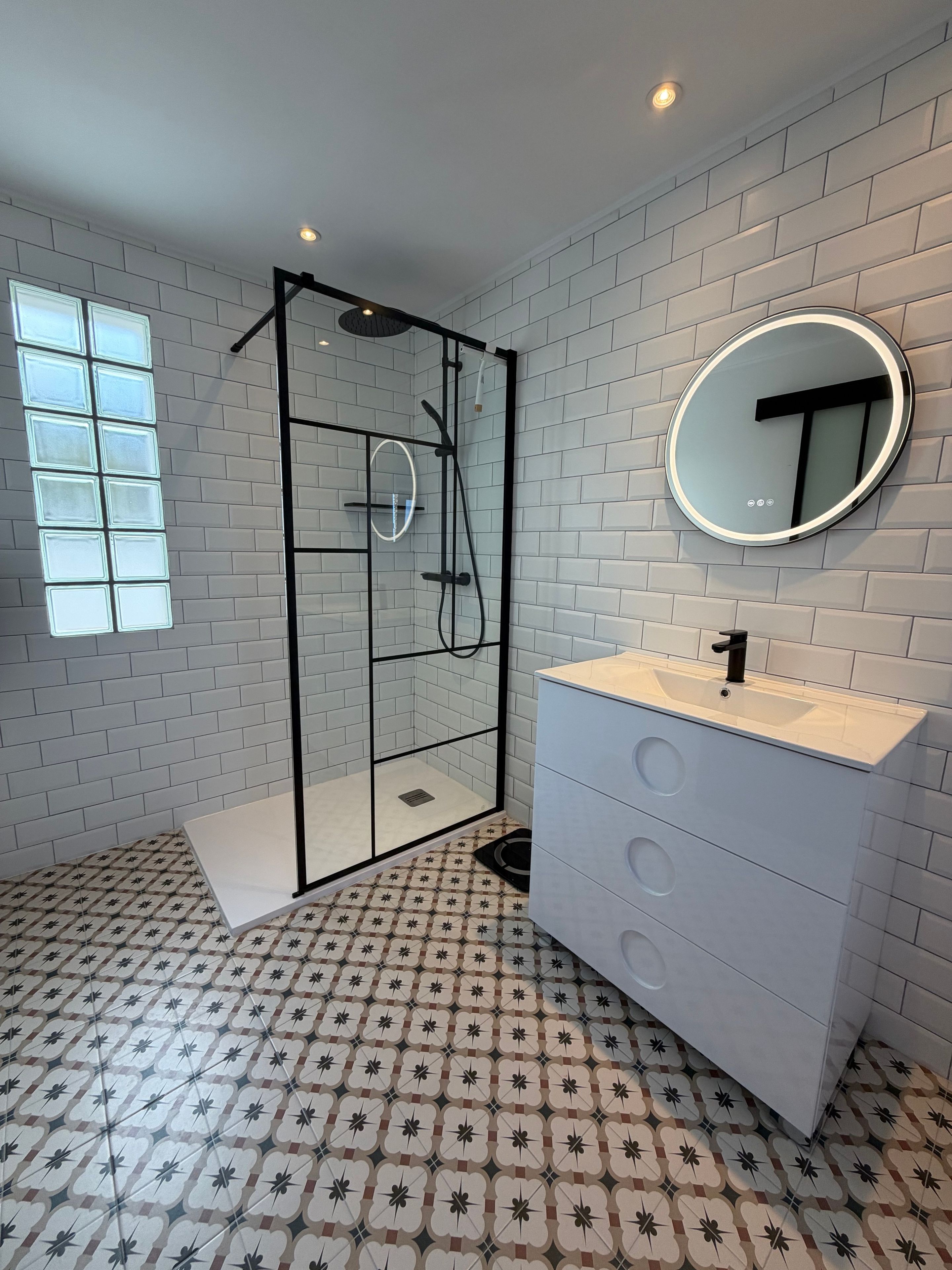 Een moderne badkamer met een douchecabine, een wastafel met spiegel en vloertegels met een patroon.