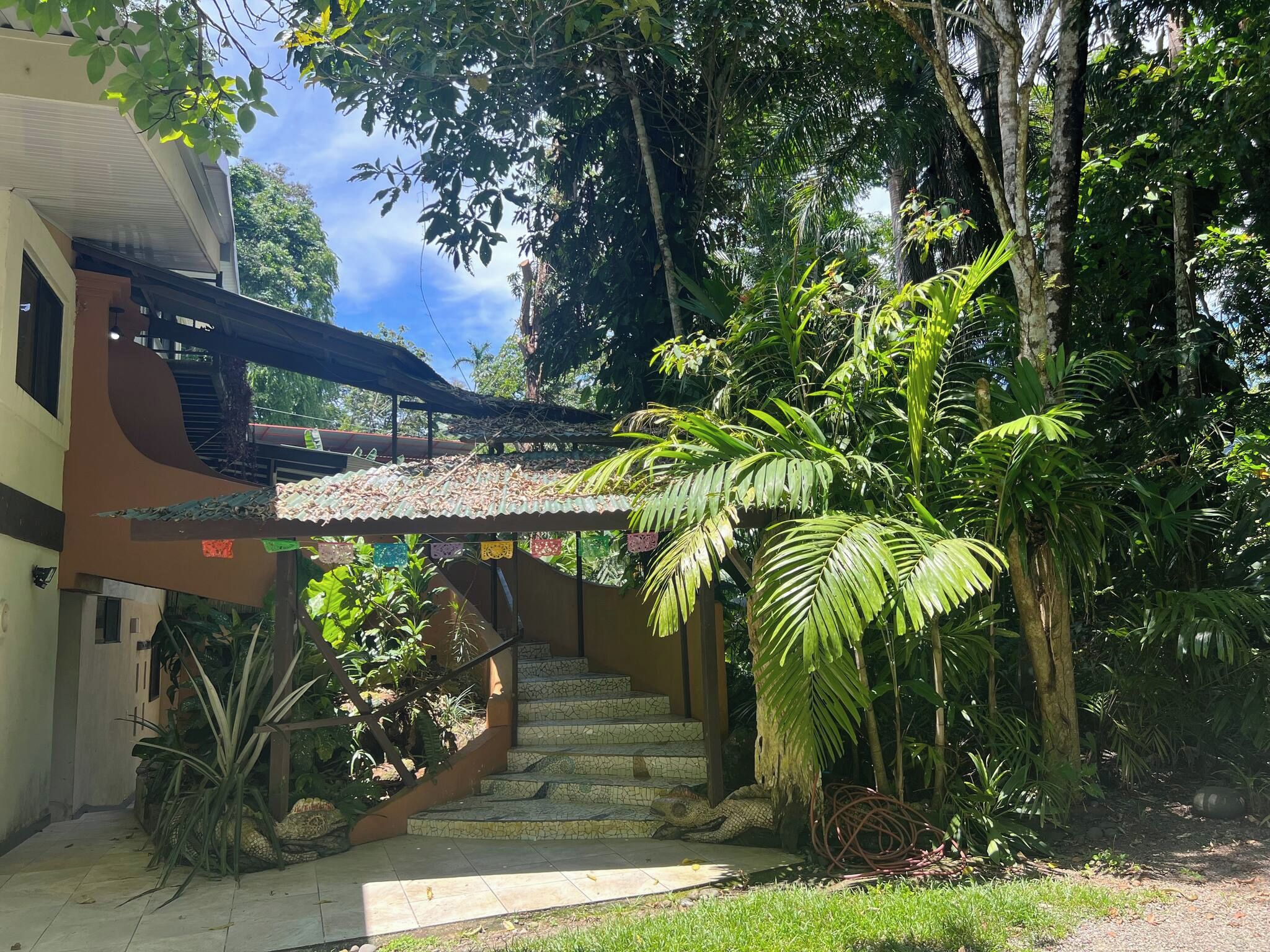 Una escalera conduce a un espacio cubierto con vistas a una exuberante vegetación y un edificio de techo inclinado.