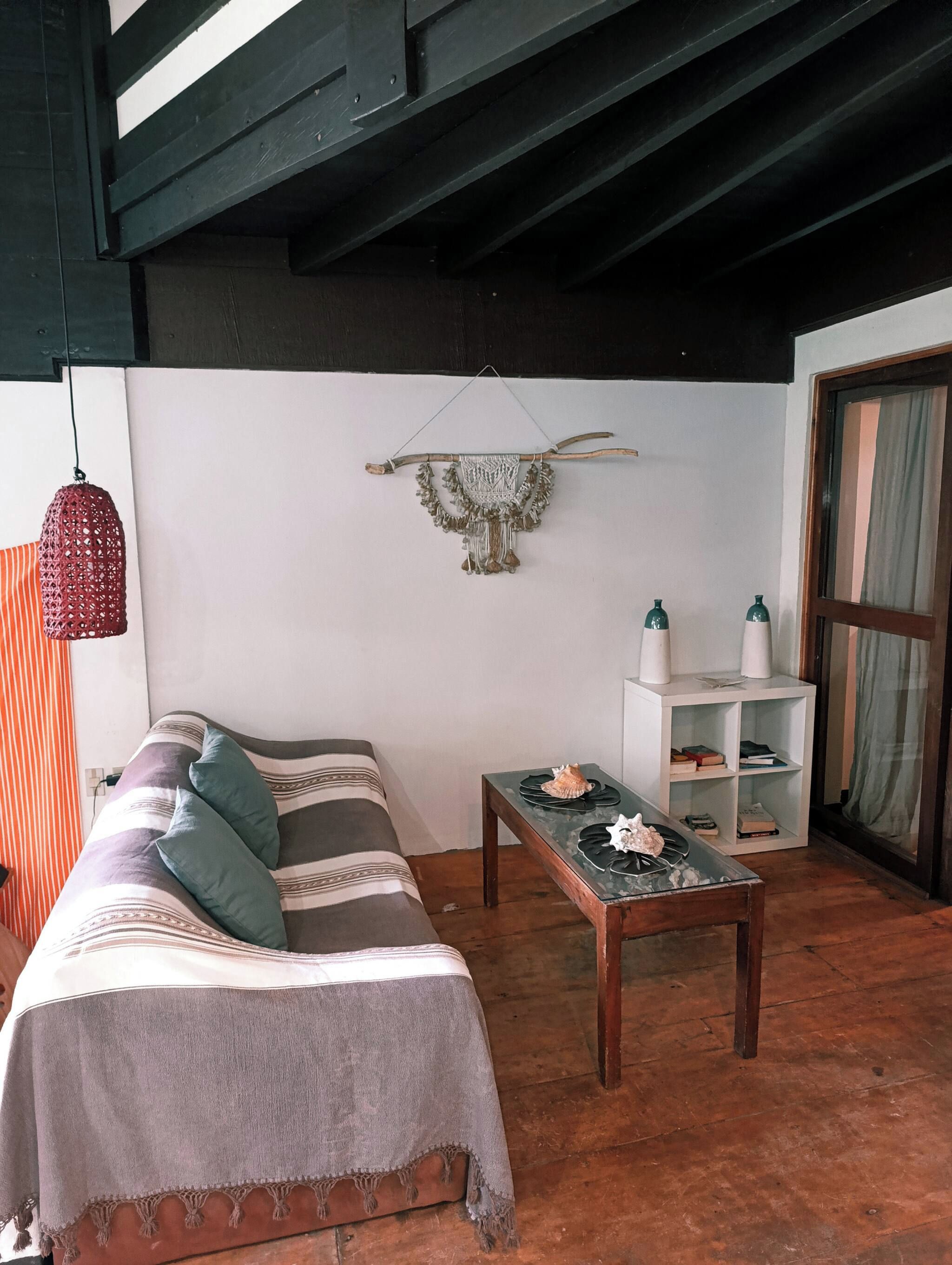 Una habitación acogedora con un sofá a rayas, una mesita con adornos, una lámpara colgante y un adorno en la pared.