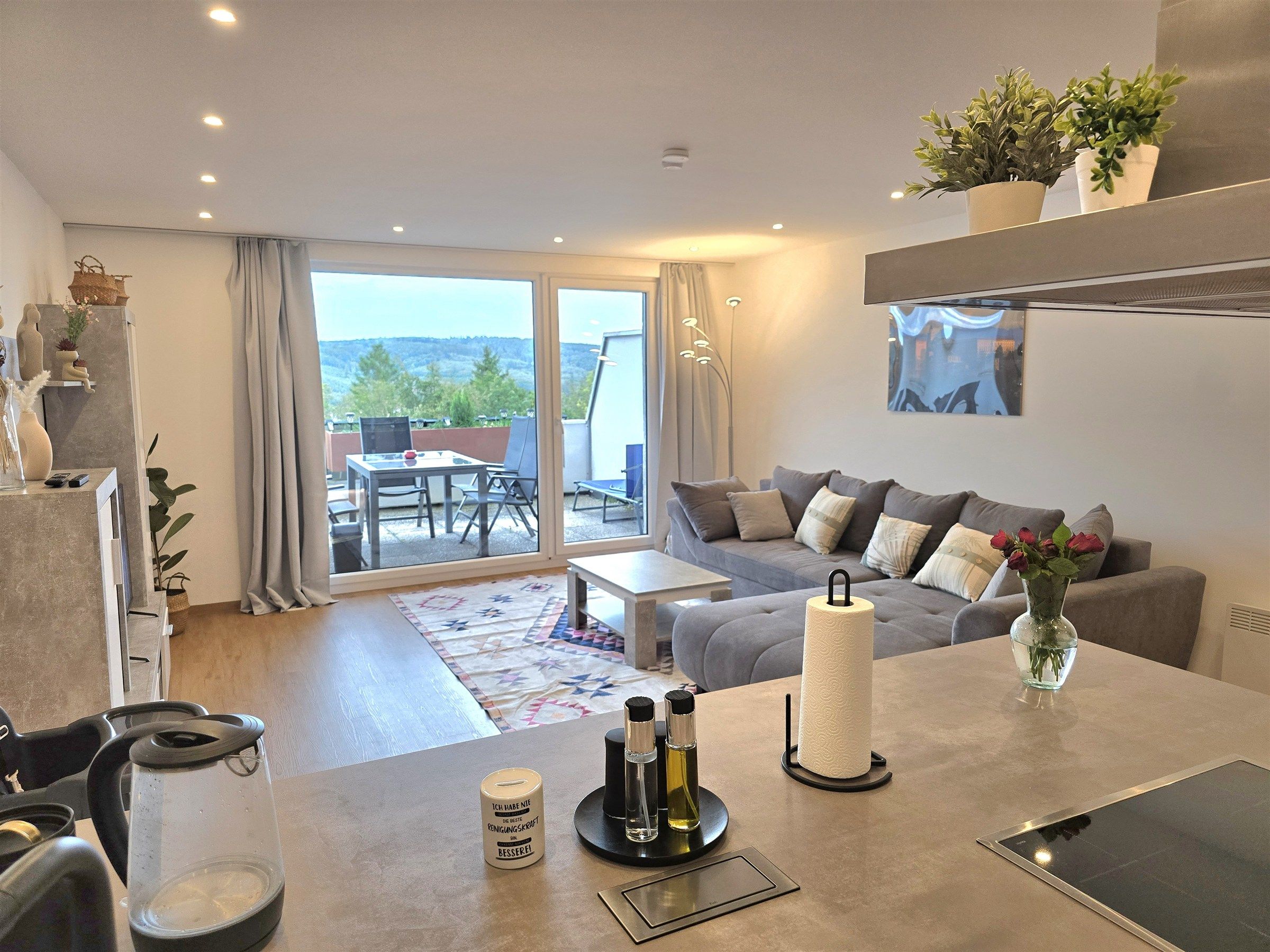 A modern living room with a sofa, a dining area, and a view of the outdoors.