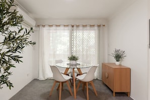 Un comedor con una mesa de vidrio, cuatro sillas, un armario de madera y una planta en maceta.