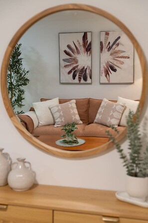 A round mirror reflecting a brown sofa with patterned cushions, a small plant on a wooden table, and two framed feather artworks on the wall. - Pyrmont 1BR | Walk to ICC & Darling Harbour (Pyrmont)