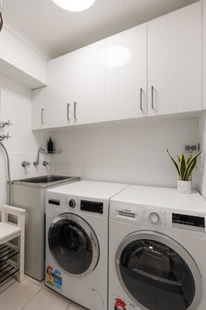 A compact laundry area with two front-loading washing machines, a sink, and cabinets. - Pyrmont 1BR | Walk to ICC & Darling Harbour (Pyrmont)