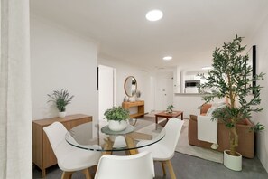 A modern interior with a glass dining table surrounded by white chairs, a wooden cabinet, and a potted plant. - Pyrmont 1BR | Walk to ICC & Darling Harbour (Pyrmont)