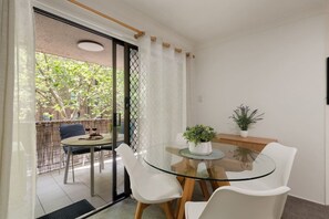 A glass-top dining table with white chairs, a potted plant, and a view of a balcony with a chair and table set for two. - Pyrmont 1BR | Walk to ICC & Darling Harbour (Pyrmont)
