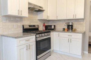 A kitchen with white cabinets, a stainless steel stove, a microwave, and a coffee maker. - Fort Worth 3BR • King Bed • Near TCU & Downtown (Fort Worth)