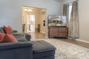 A living room with a dark-colored sofa, a flat-screen TV on a wooden stand, and a patterned rug. - Fort Worth 3BR • King Bed • Near TCU & Downtown (Fort Worth)