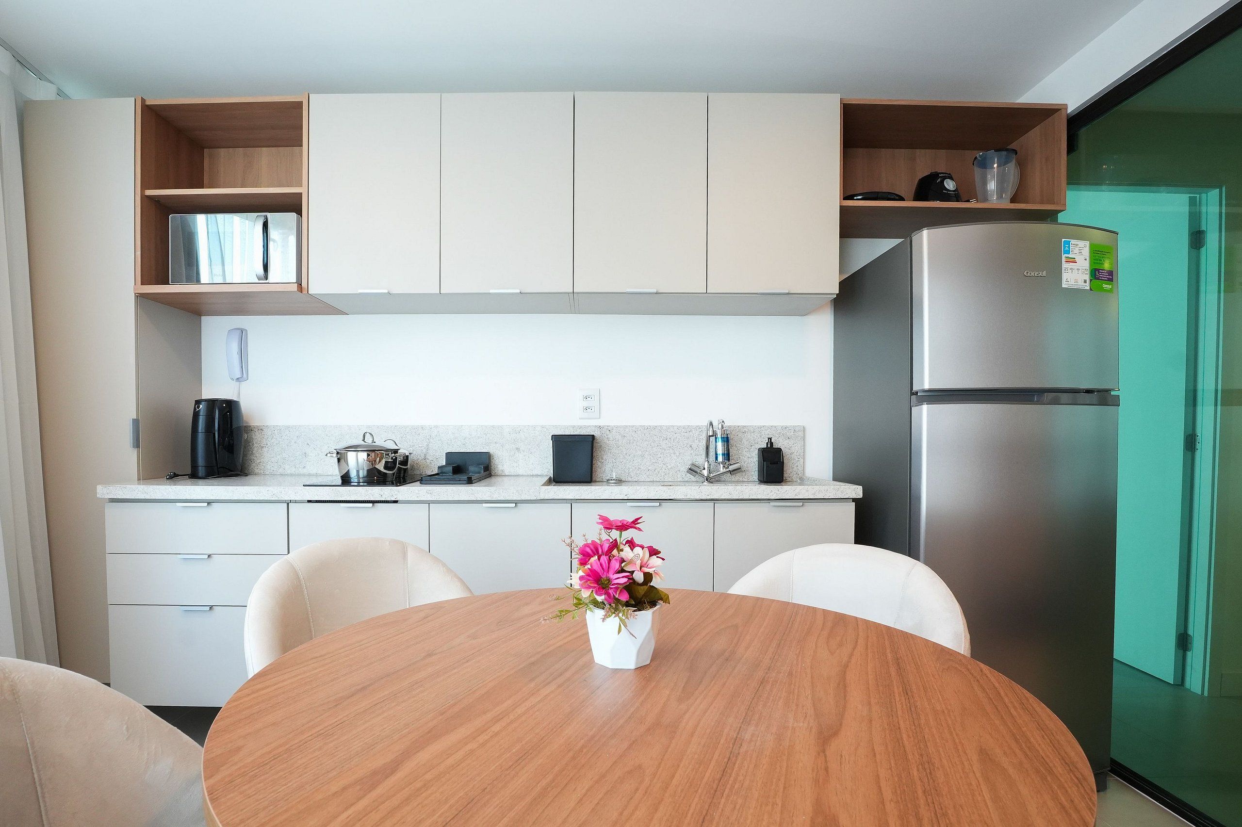 A modern kitchen with a round dining table, chairs, a refrigerator, and a coffee maker.