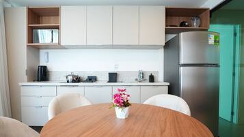 A modern kitchen with a round dining table, chairs, a refrigerator, and a coffee maker.