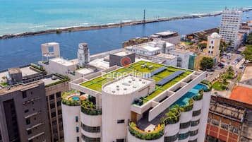 A high-rise building with a rooftop garden, a swimming pool, and a view of the sea.