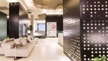 A modern interior with a white sofa, a reception desk, and perforated metal panels.