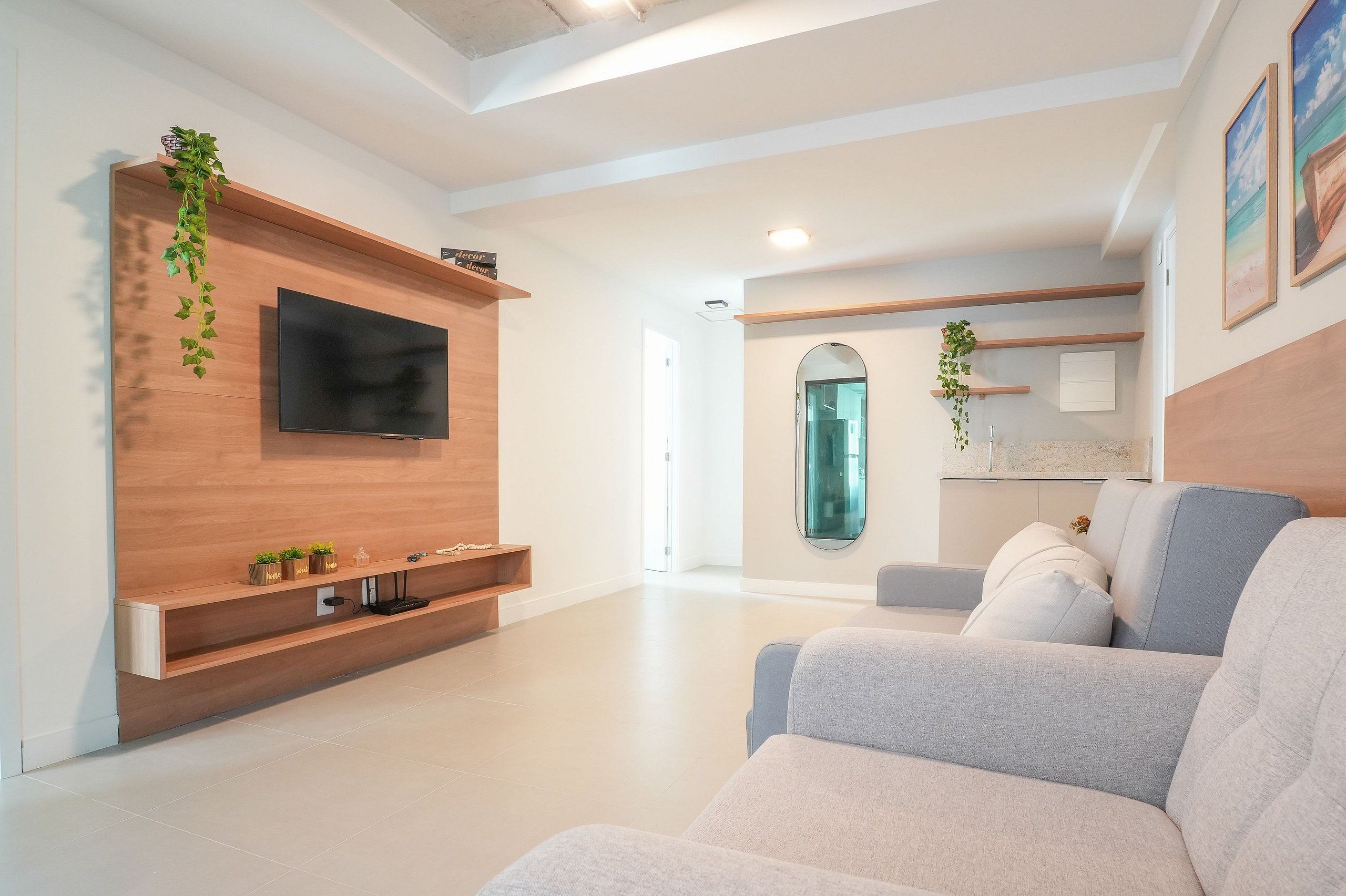 A modern living room with a flat-screen TV mounted on a wooden wall, a grey sofa, and a small coffee table.