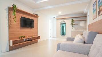 A modern living room with a flat-screen TV mounted on a wooden wall, a grey sofa, and a small coffee table.