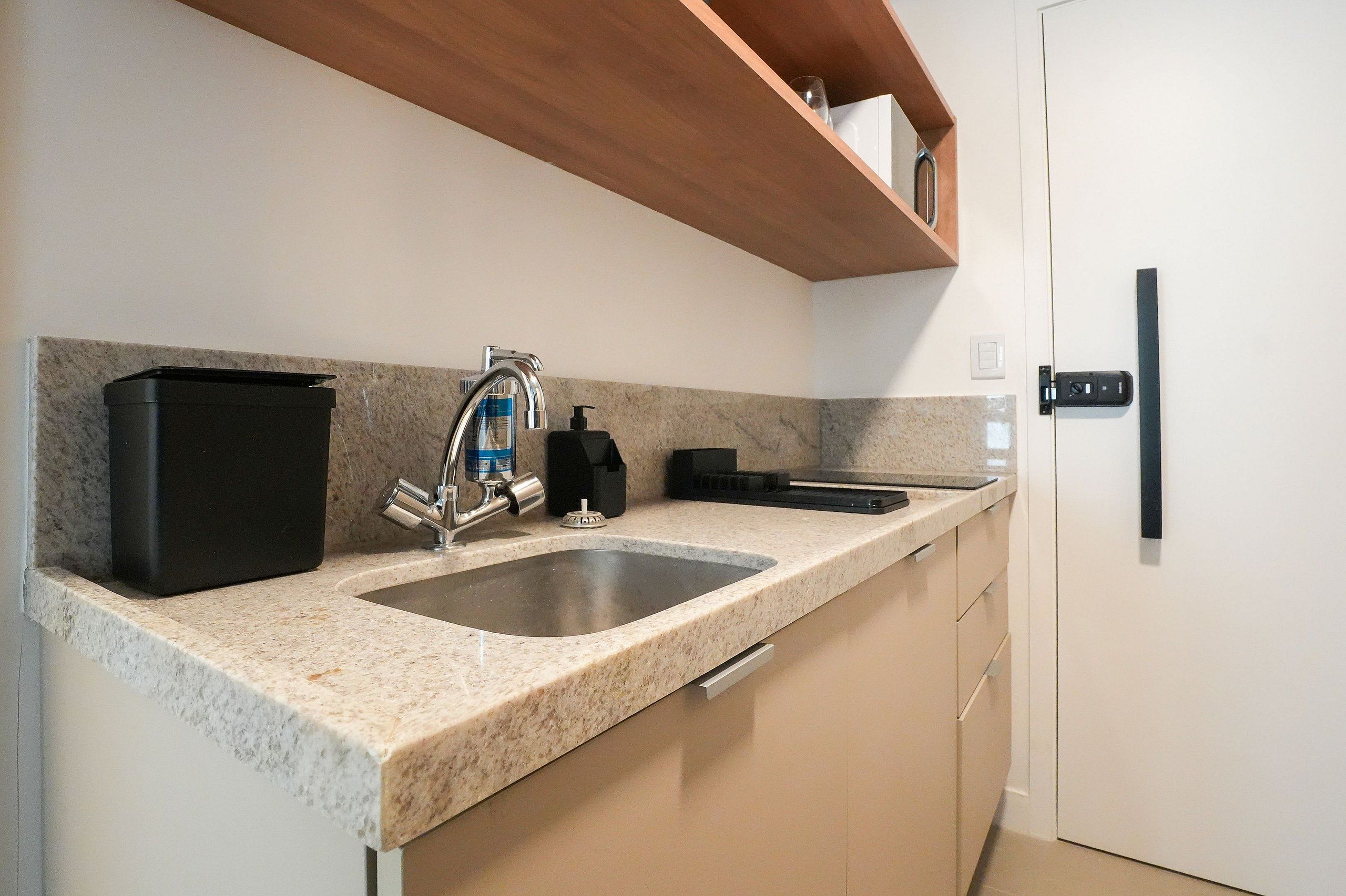 Una cocina con un lavamanos doble, un grifo de acero inoxidable, un dispensador de jabón negro y un microondas.