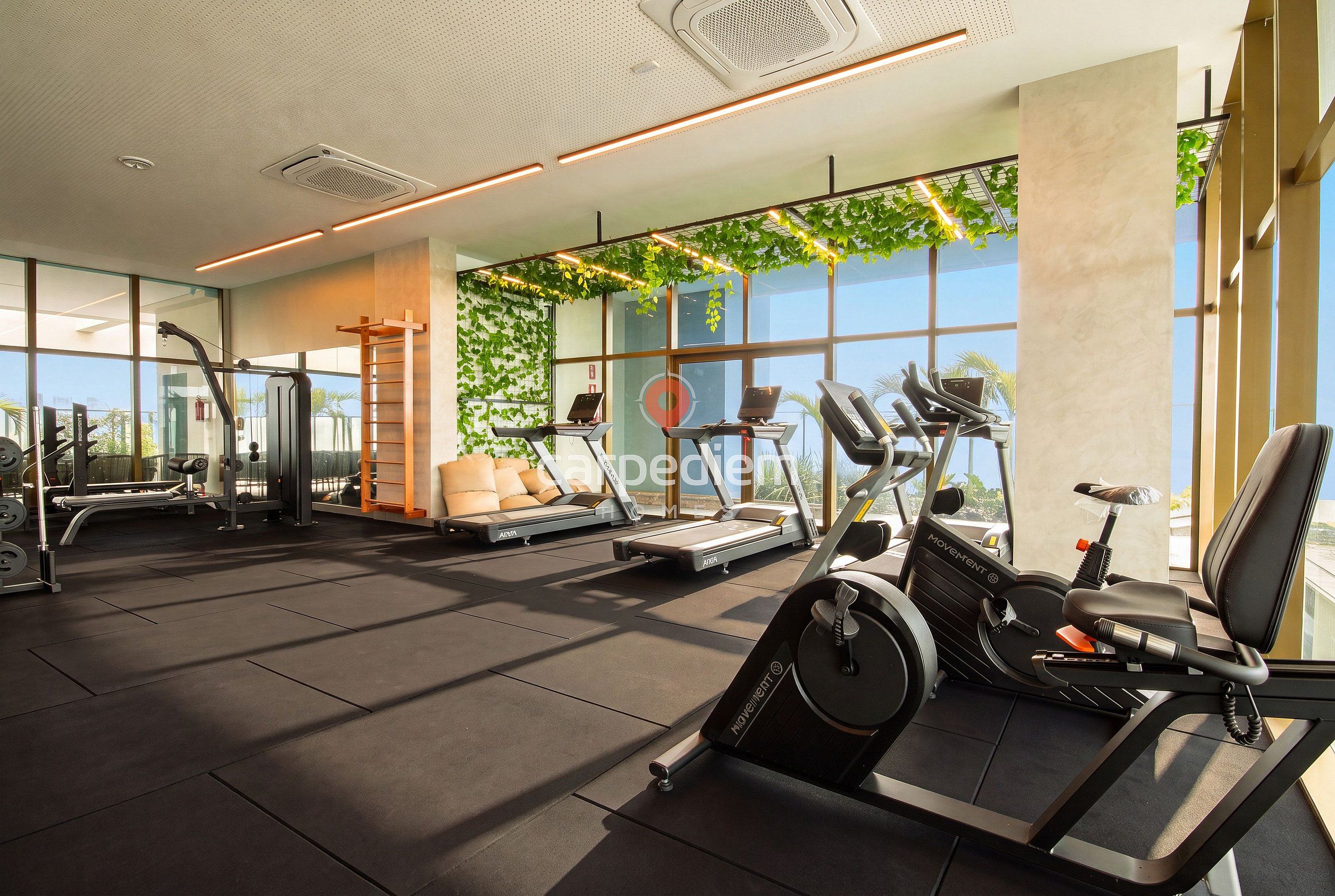 A modern gym with various exercise equipment, large windows, and a view of the outdoors.