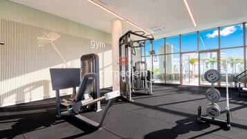 Un gimnasio con equipo de ejercicio, ventanas amplias y vistas a palmeras.