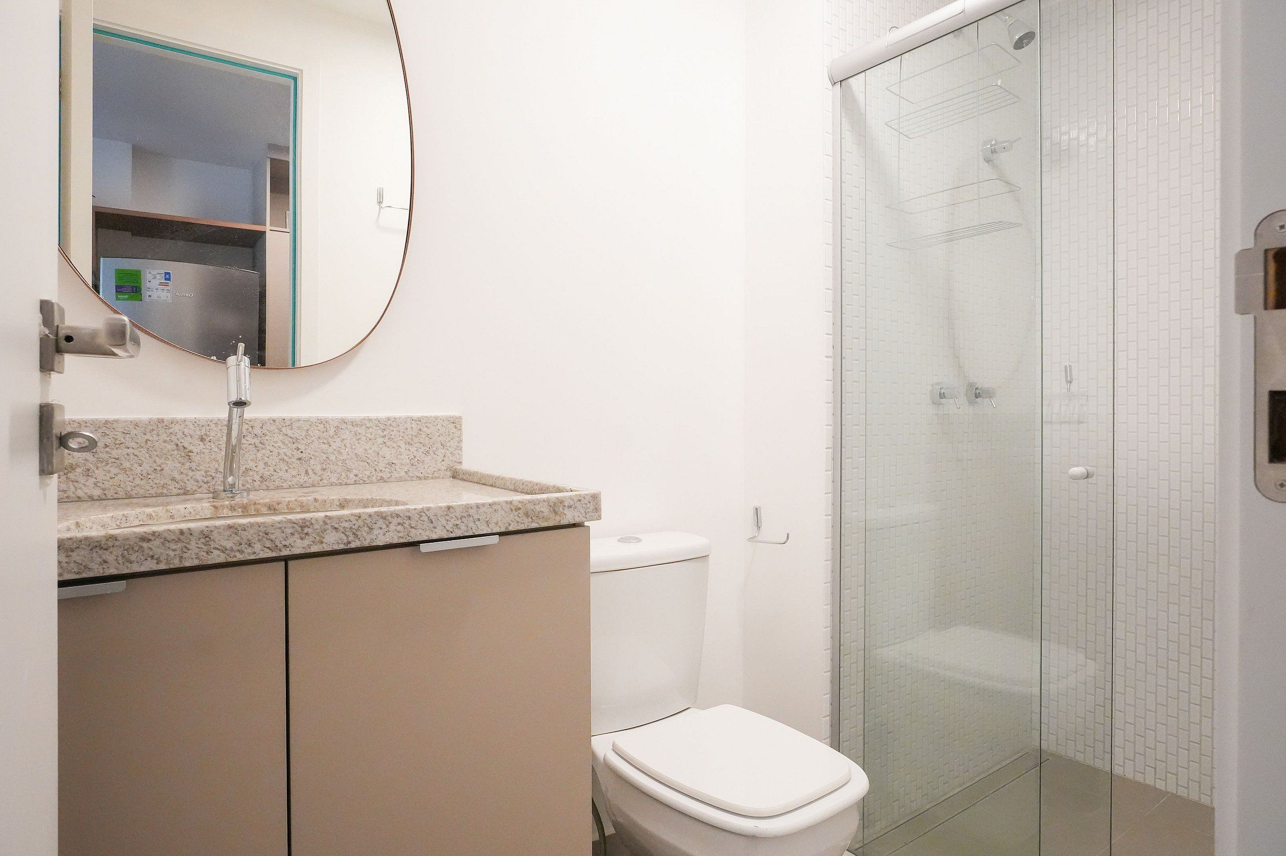 Ein Badezimmer mit Granitplatte, Toilette, einer Duschkabine aus Glas und einem Spiegel mit türkisem Rahmen.