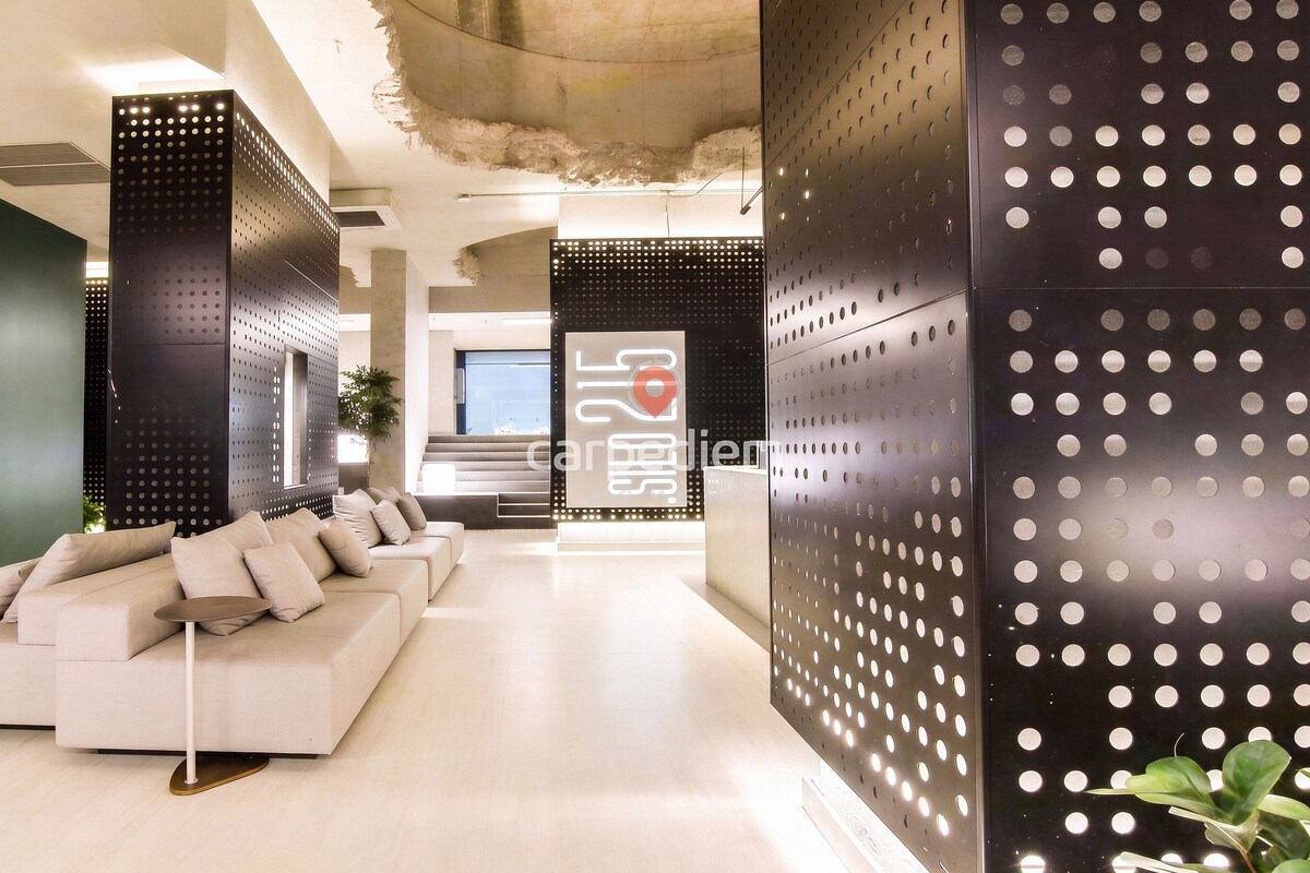 A modern interior with a white sofa, a reception desk, and perforated metal panels.