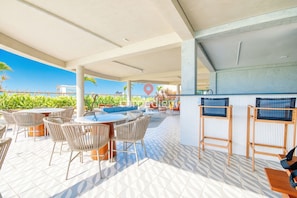 An outdoor patio area with round tables and wicker chairs, a bar area with stools, and a view of the city skyline.