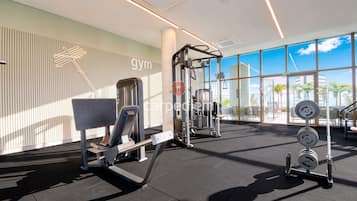 Une salle de sport équipée de matériel d’exercice, dotée de grandes fenêtres et offrant une vue sur des palmiers.