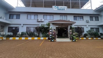 A hotel with a sign reading 'The Orchid Grand Hotel.' It features a covered entrance, multiple windows, and air conditioning units.