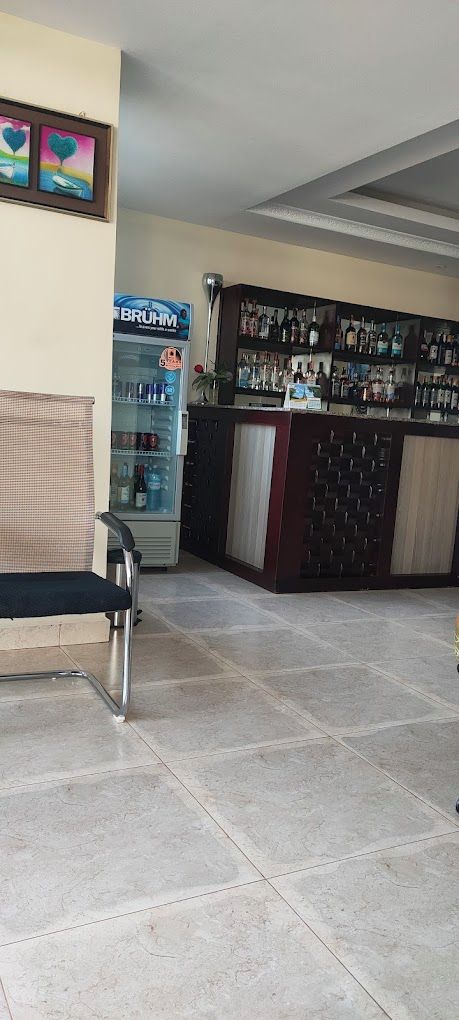 Un coin bar équipé d’un réfrigérateur rempli de boissons, un espace détente avec un fauteuil et un sol carrelé.